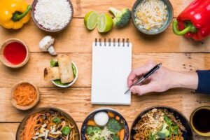 person-writing-notepad-with-pen-traditional-thai-food-wooden-table